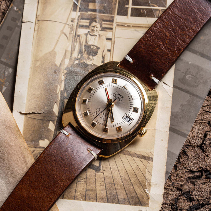 flatlay of the 1975 Timex Electric Dynabeat Time Zone, on a background of vintage photos