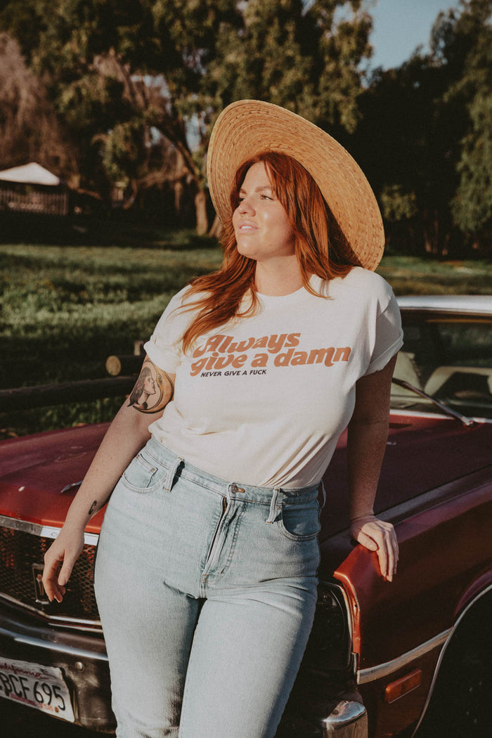 Woman leaning on a car in a sunhat wearing White Always Give a Damn Shirt in Unisex by The Bee and The Fox