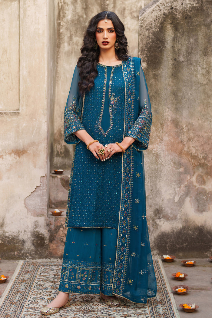 Woman in a blue traditional outfit standing against a textured wall.