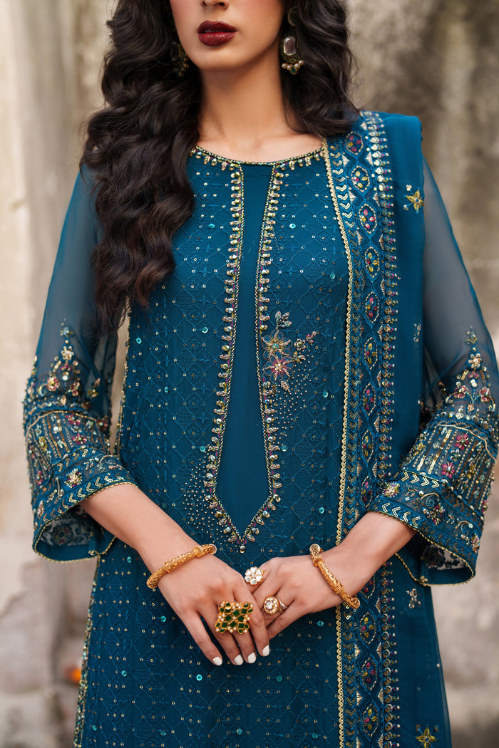 Woman wearing a teal embroidered traditional outfit with jewelry.