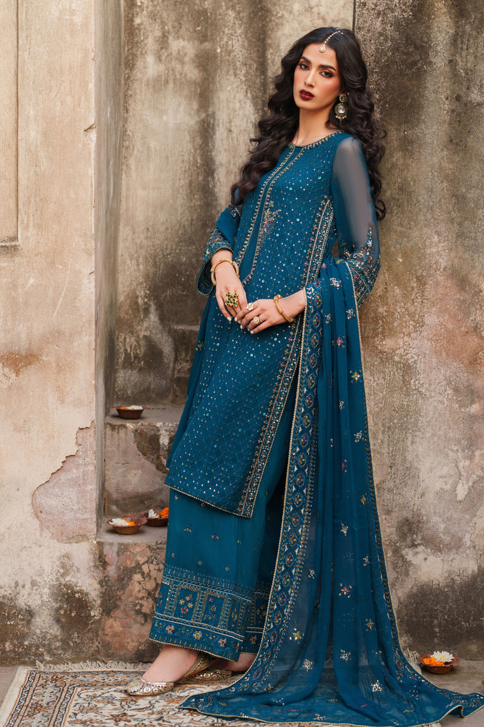 Woman in a blue traditional outfit standing against a textured wall.