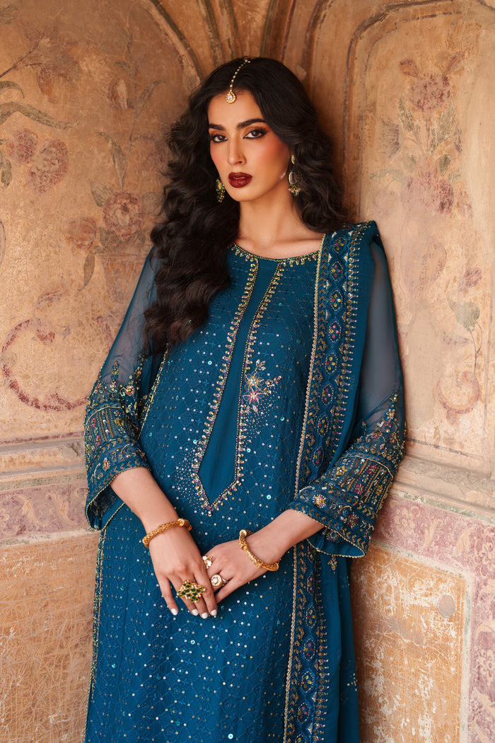 Woman in a blue traditional outfit standing against an ornate wall.