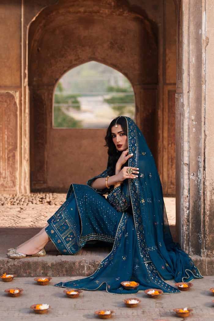 Woman in a blue traditional outfit sitting under an archway with candles around her.