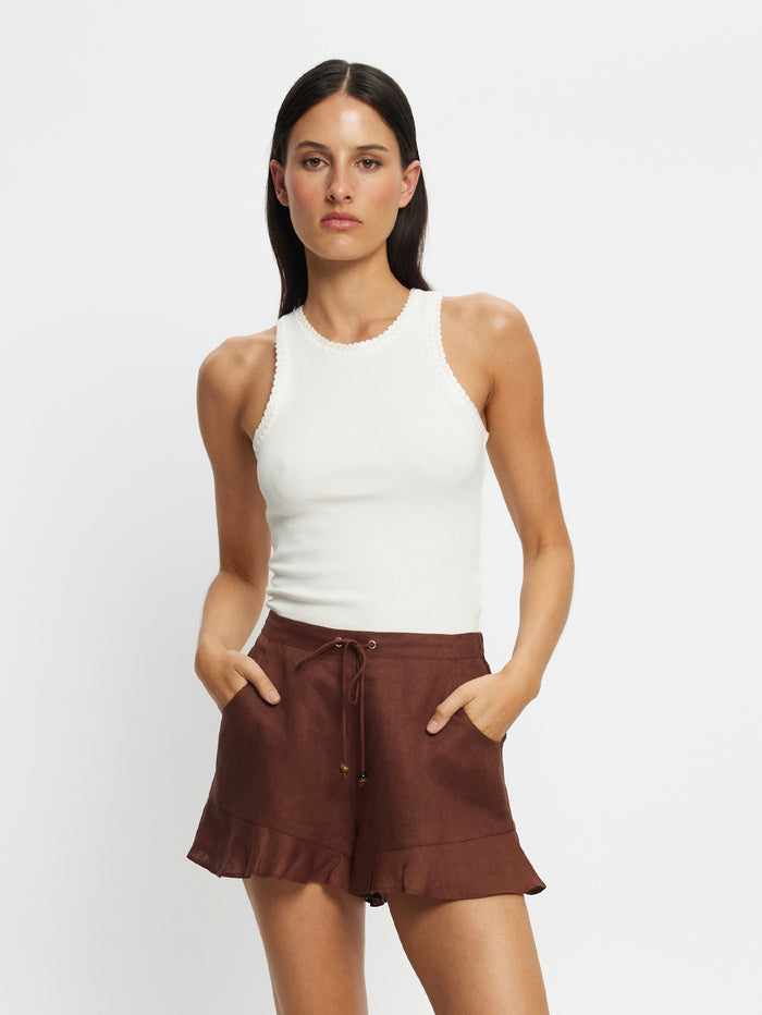 Woman wearing a white sleeveless top and brown shorts on a light gray background