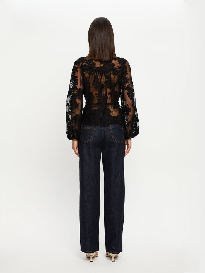 Person wearing a black lace top and dark jeans on a white background