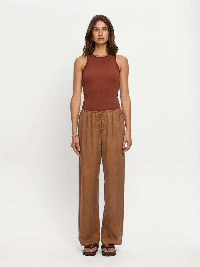 Woman wearing a rust-colored sleeveless top and brown wide-leg pants on a white background