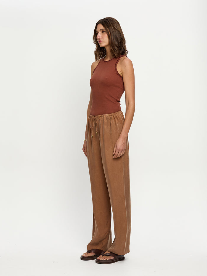Woman wearing a brown sleeveless top and tan pants on a white background