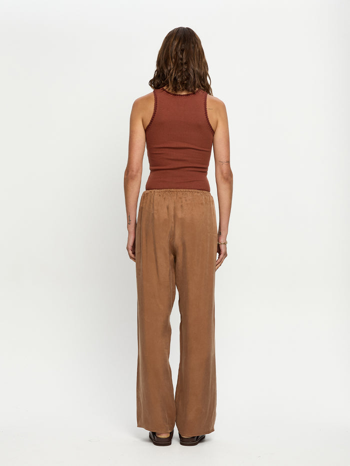 Woman wearing a brown tank top and wide-leg pants on a white background