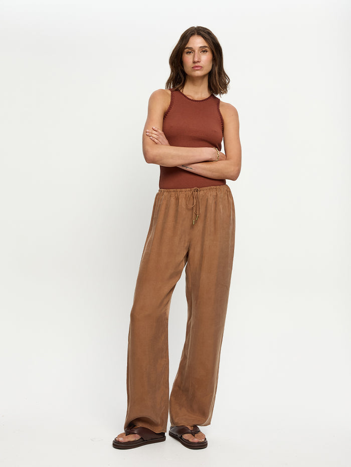 Woman wearing a brown sleeveless top and tan pants on a white background