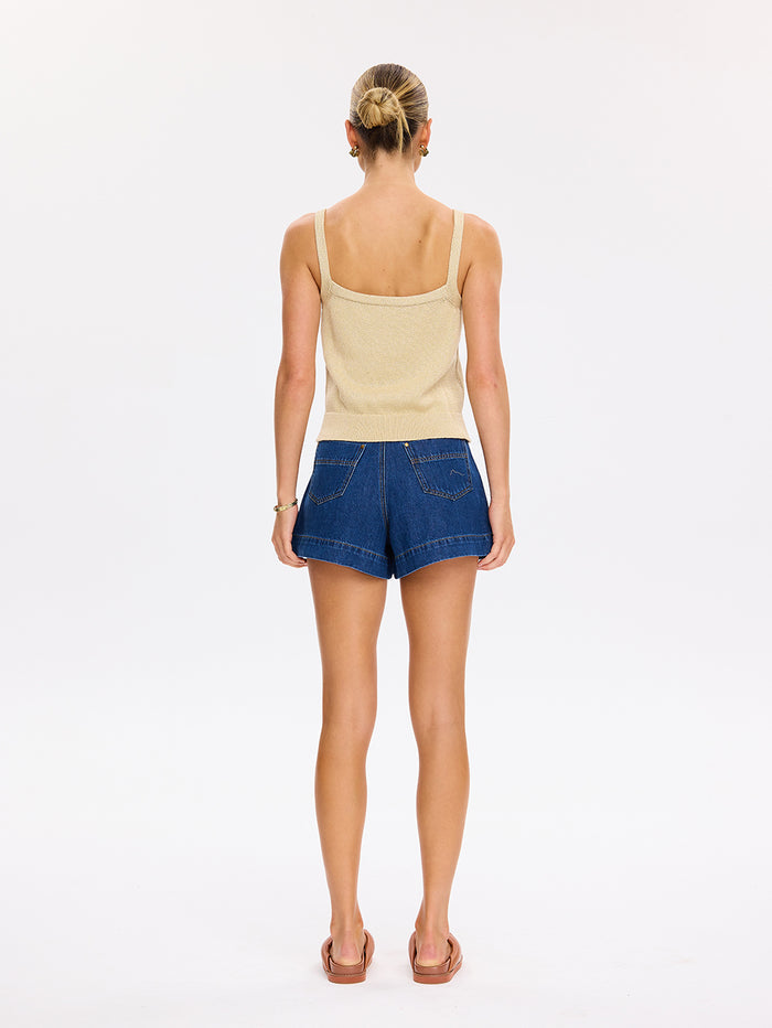 Woman wearing a beige tank top and blue denim shorts on a white background