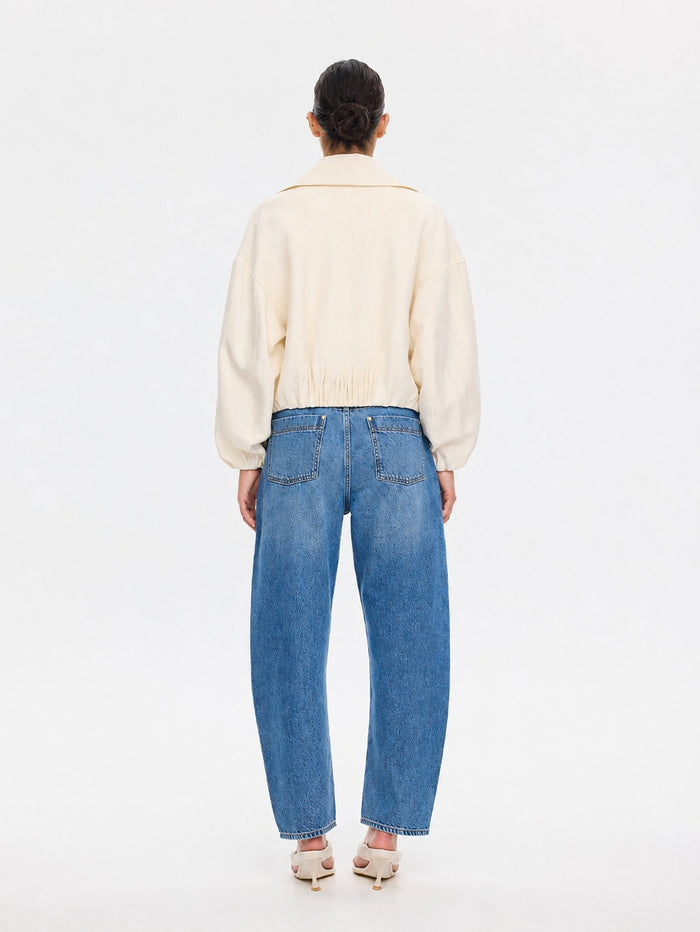 A model viewed from the back wearing a cream-colored cropped jacket and wide-leg blue jeans, standing against a plain white studio background.