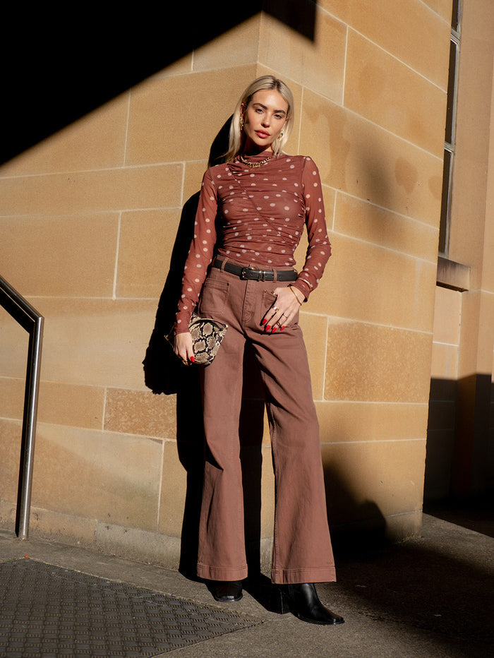 KIVARI influencer lifestyle shot - model wearing brown polka dot mesh long-sleeve top with brown wide-leg trousers and snake-print bag