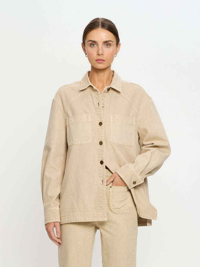 Woman wearing a beige denim shirt and jeans on a white background