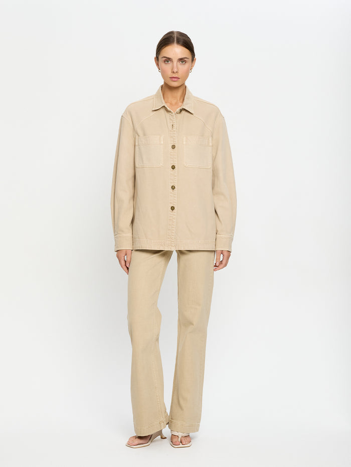 Woman wearing a beige denim shirt and jeans on a white background