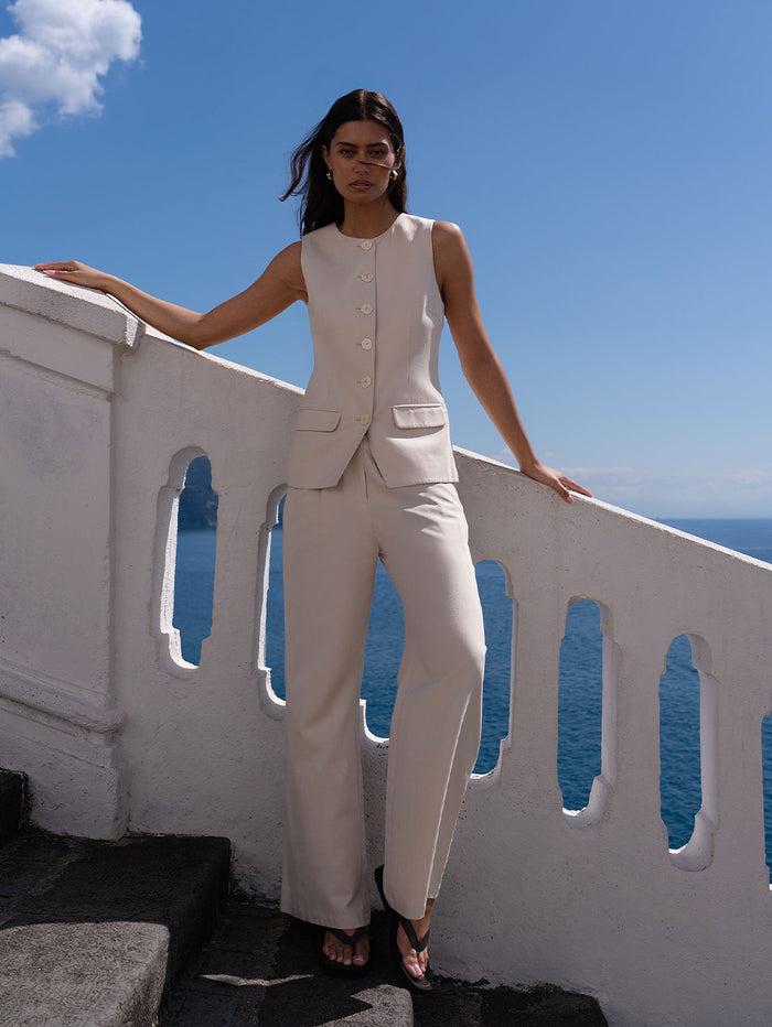 Woman on stairs by railing wearing beige vest and trousers