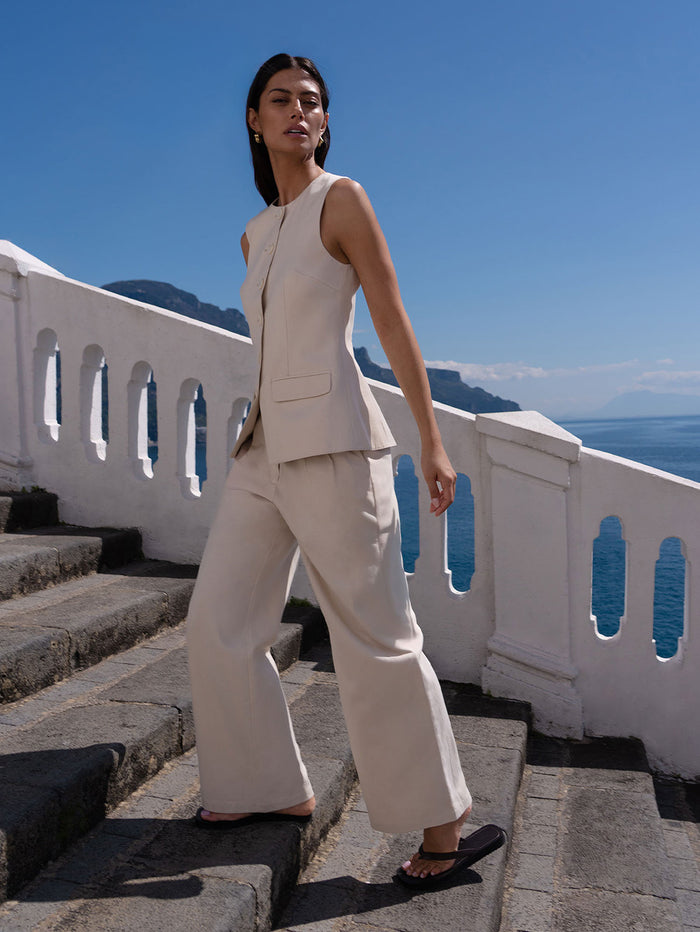 Woman in a beige suit standing on stone steps with ocean view