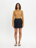 Woman wearing a mustard yellow top and dark denim skirt on a white background
