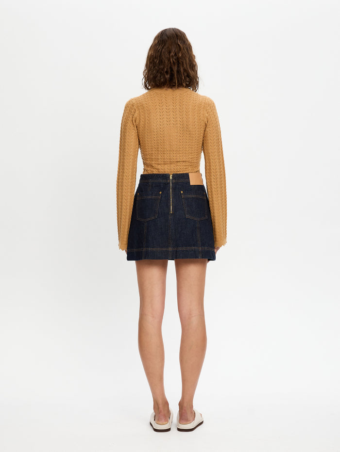 Woman wearing a mustard yellow checkered top and dark denim skirt on a white background