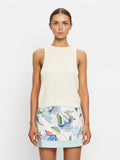 Woman wearing a white sleeveless top and floral skirt on a plain background