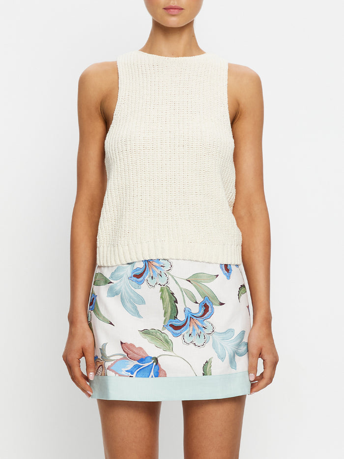 Woman wearing a cream sleeveless top and floral skirt on a white background