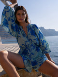 Woman wearing a blue floral dress sitting by a body of water.
