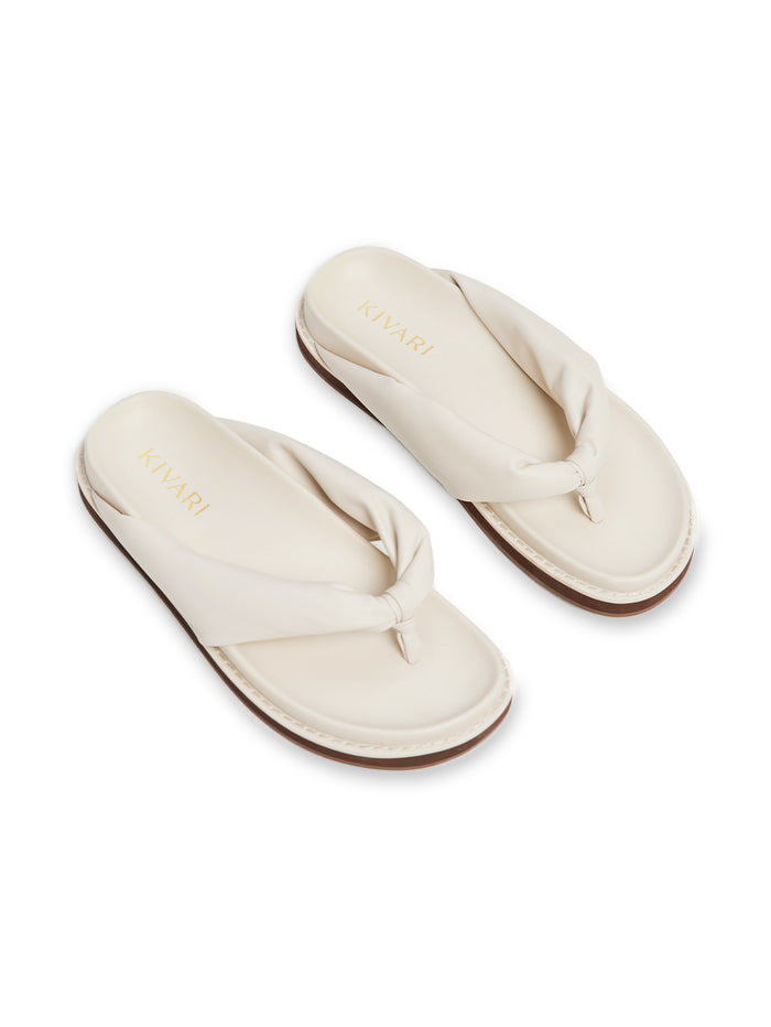 Pair of cream-colored slides with a knot design on a white background