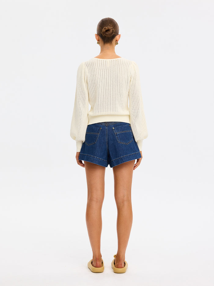 Person wearing a white sweater and blue denim shorts on a plain background