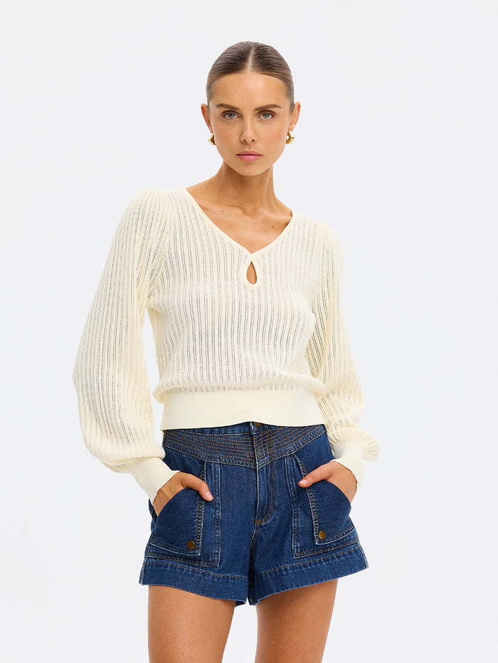 Woman wearing a cream sweater and blue shorts on a white background