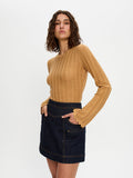 Woman wearing a mustard yellow sweater and dark denim skirt on a white background