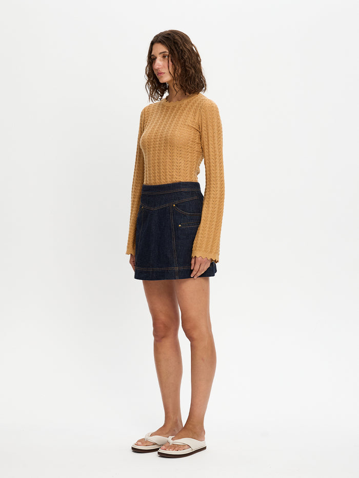 Woman wearing a mustard yellow sweater and dark denim skirt on a white background