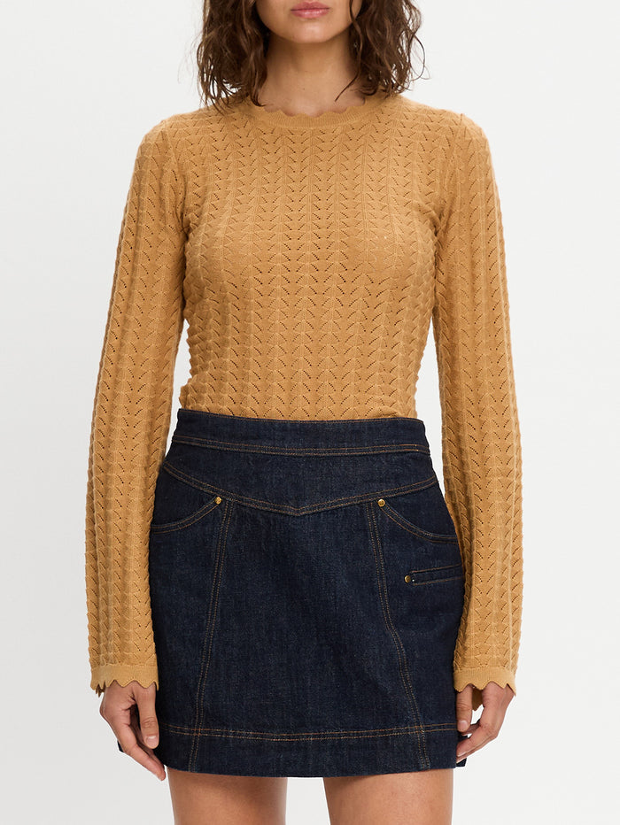 Person wearing a mustard yellow cable knit sweater and dark blue denim skirt on a white background