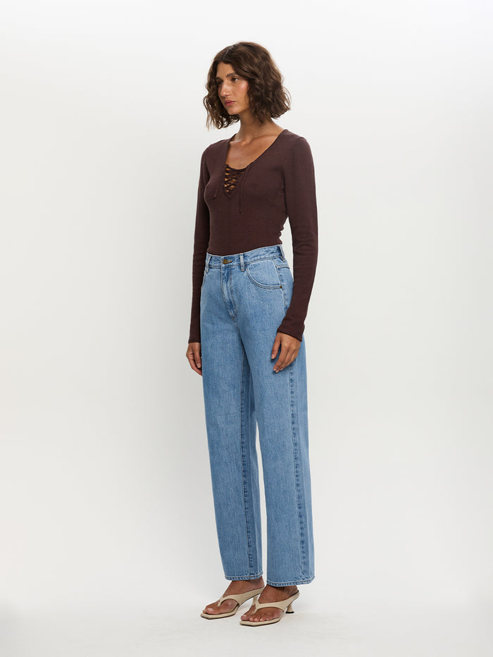Woman wearing a brown long-sleeve top and blue jeans on a white background