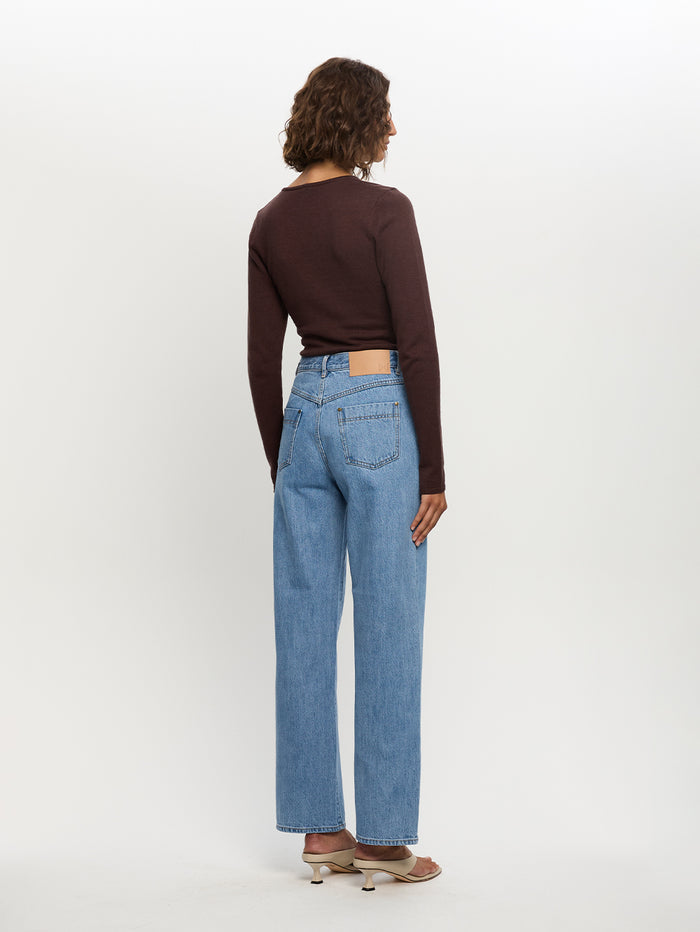 Person wearing a brown long-sleeve top and light blue jeans on a white background
