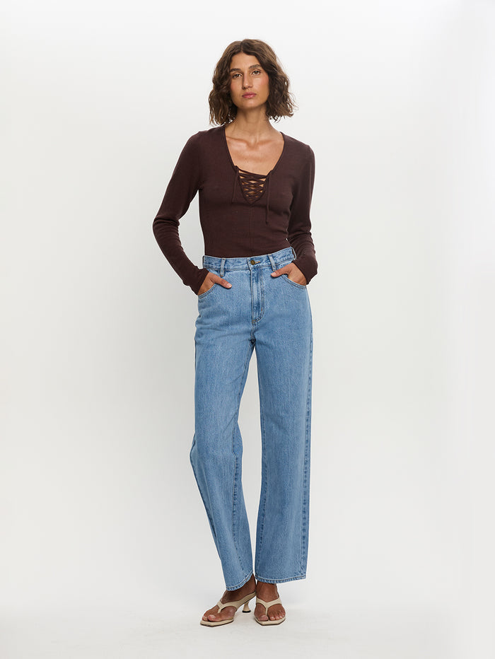Woman wearing a brown top and blue jeans on a white background