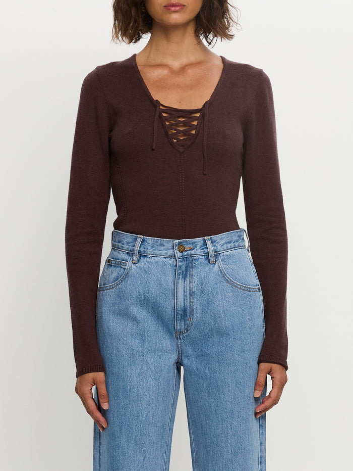 Person wearing a brown long-sleeve top with lace-up front and blue jeans on a white background
