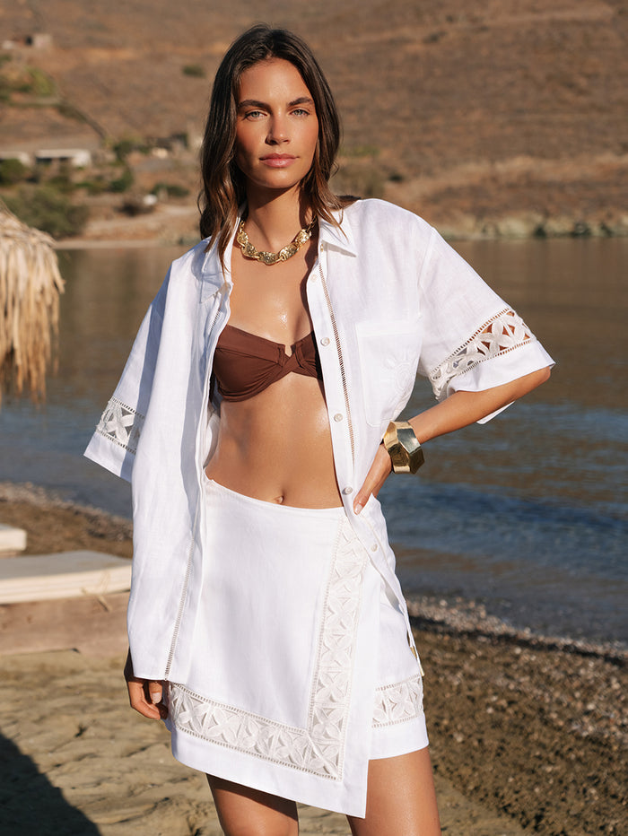Woman in a white cover-up and brown bikini standing on a beach.