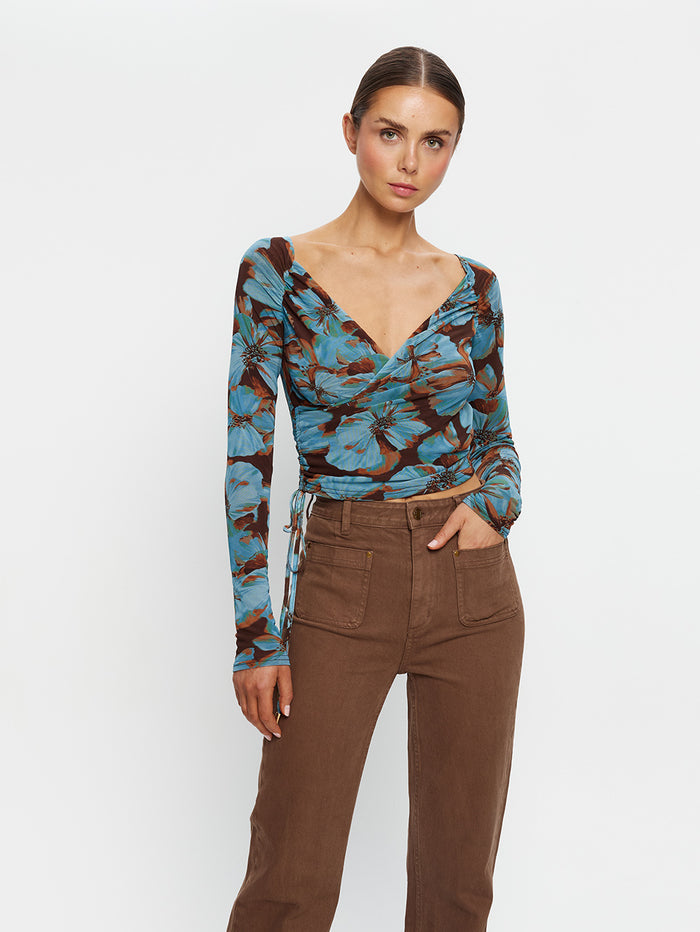 KIVARI Nieve Mesh Top in Blue Floral Print – three-quarter view showing drawstring hem, model wearing women's long-sleeve wrap mesh top with brown pants