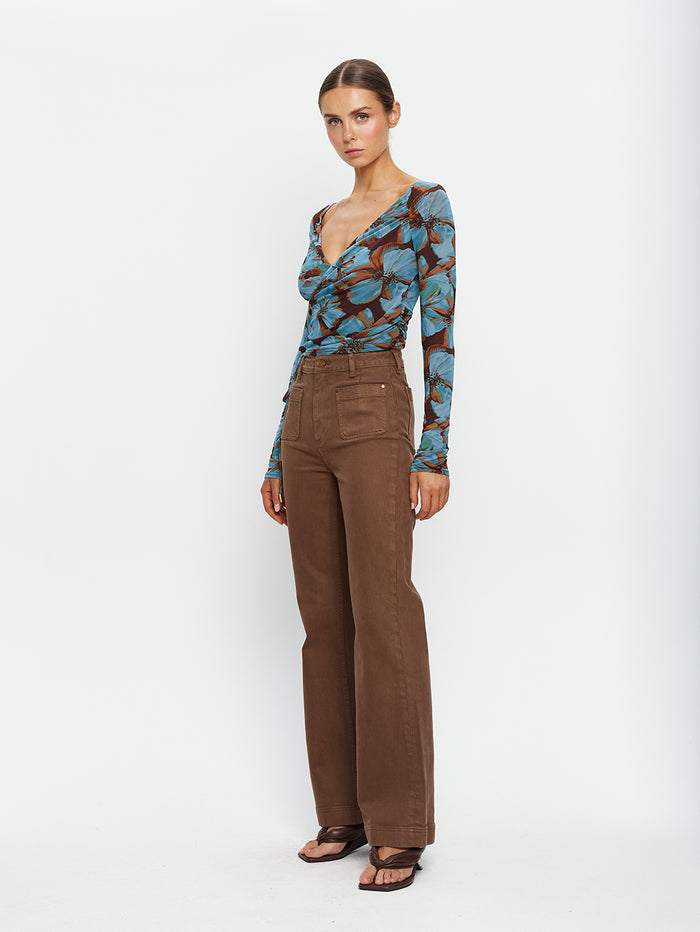 KIVARI Nieve Mesh Top in Blue Floral Print – full-length diagonal view of model wearing women's long-sleeve wrap mesh top with brown flare pants