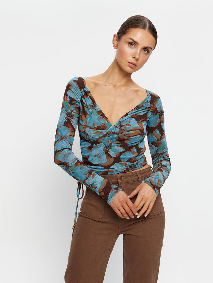 KIVARI Nieve Mesh Top in Blue Floral Print – model wearing women's long-sleeve wrap mesh top, clasped hands pose