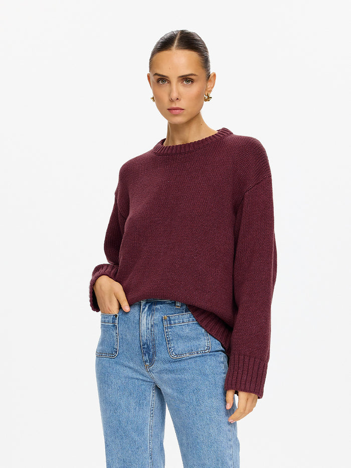 KIVARI Odette Crew Neck Jumper in Plum - cropped view of model wearing dark plum ribbed knit jumper tucked into light blue jeans