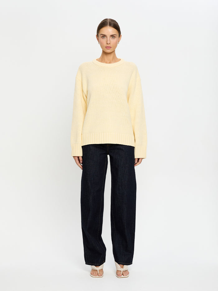 Woman wearing a light yellow sweater and navy pants on a white background