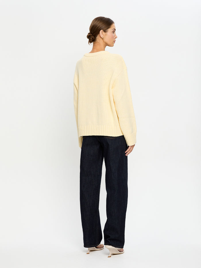 Woman wearing a light yellow sweater and dark blue jeans on a white background