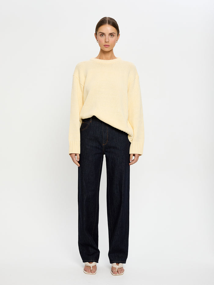 Woman wearing a yellow sweater and navy jeans on a white background