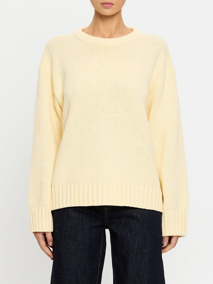 Person wearing a light yellow sweater and dark jeans on a white background