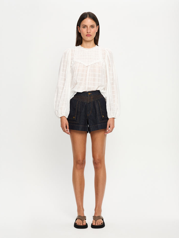 Woman wearing a white blouse and dark denim shorts on a white background