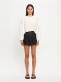 Woman wearing a white blouse and dark denim shorts on a white background