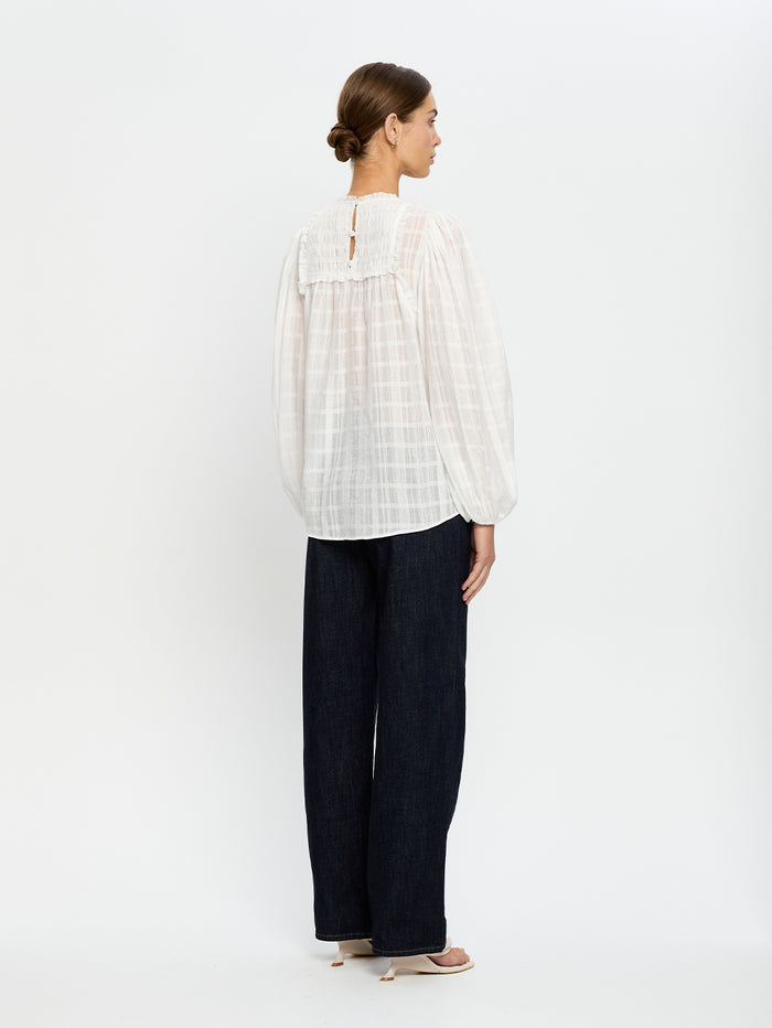 Woman wearing a white blouse and navy jeans on a white background