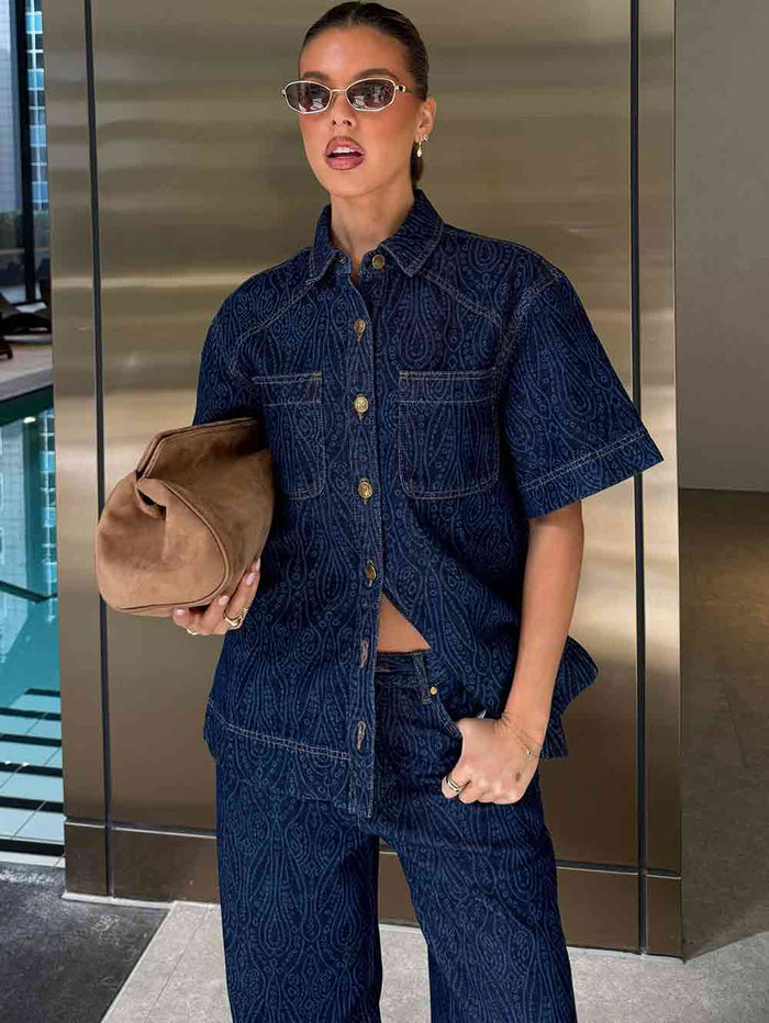Woman in a denim outfit holding a brown bag in an indoor setting.