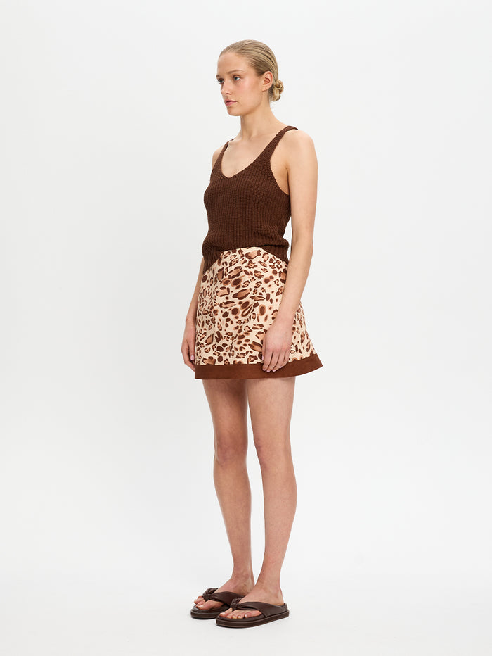 Woman wearing a brown tank top and leopard print skirt on a white background