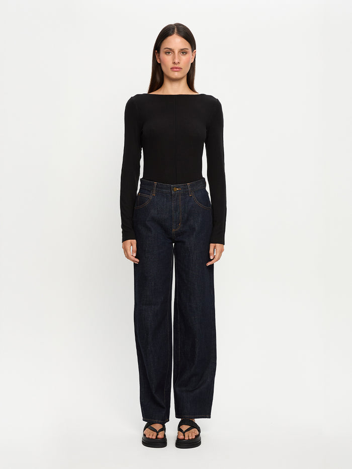 Woman wearing a black long-sleeve top and dark jeans on a white background